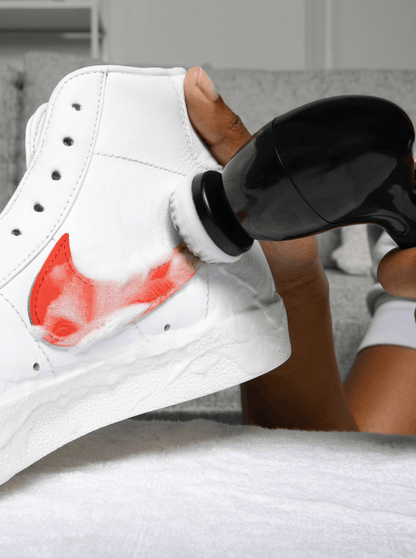 A closeup image of the Klean Kickz scrub brush cleaning a pair of white Nike sneakers